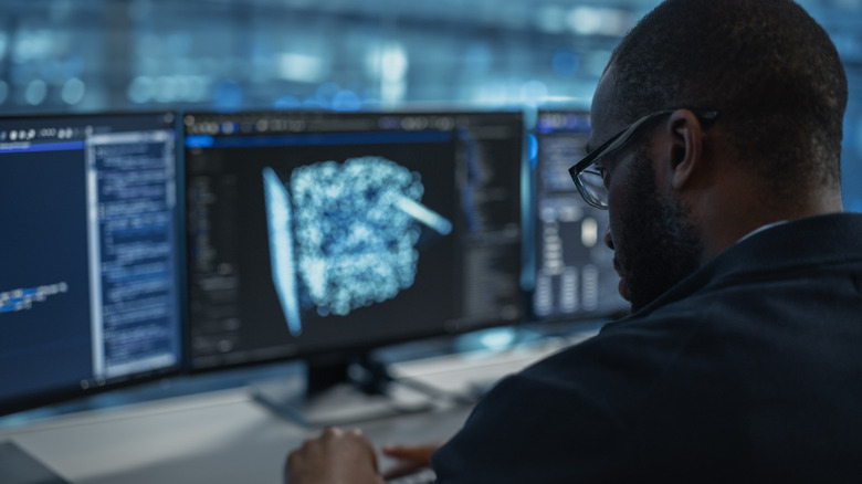 Man at desk performing computer tasks with three monitors