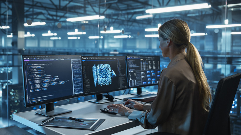 Woman performing computer tasks at desk with three monitors