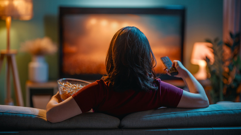 Person watching TV while holding a remote and a bowl of popcorn.
