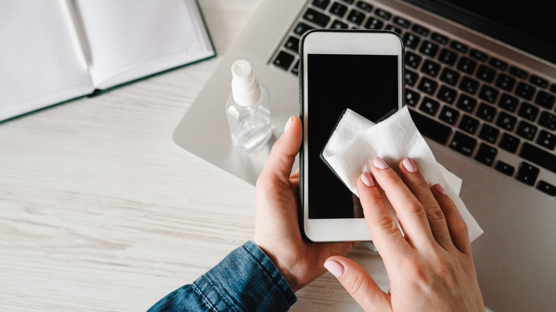 A closeup of a person cleaning a smartphone with a cloth and cleaning solution