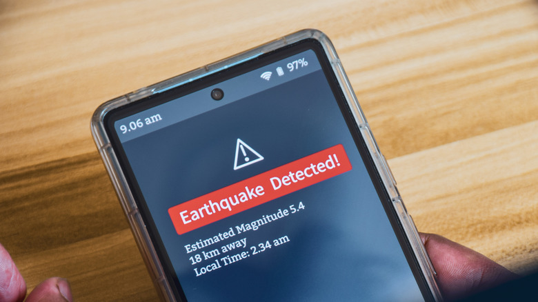 man holding phone with earthquake warning on the screen