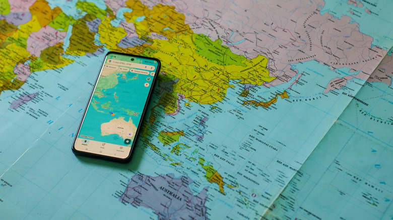 Google Maps open on a smartphone placed on a paper map of the world.