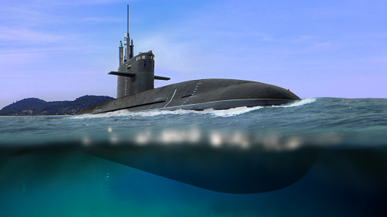 Military submarine partially surfaced with hull visible above and below the ocean waterline.