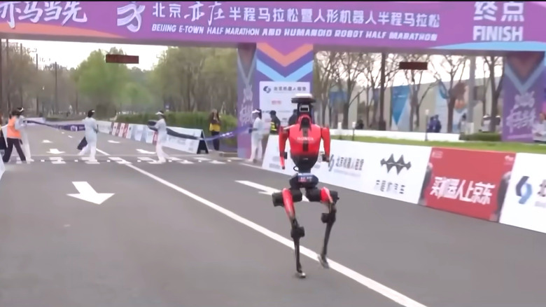 Lightning, a bright red humanoid robot with a camera pack, races through the finish line, breaking the half-marathon record.