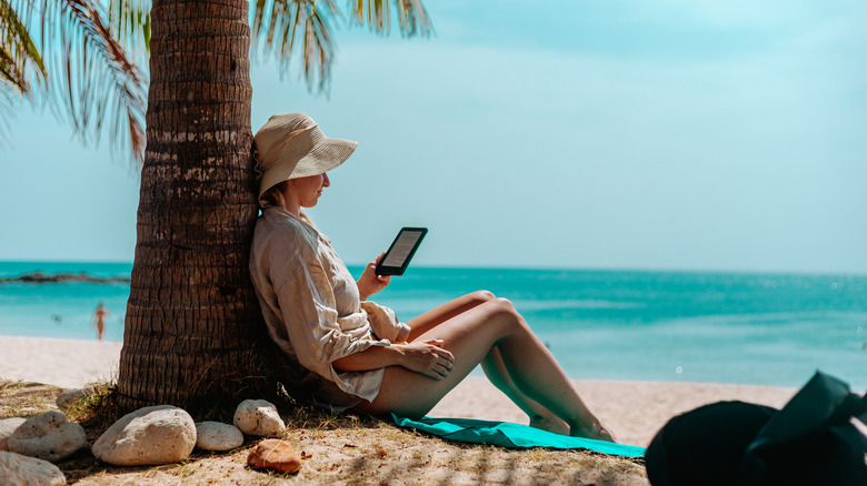 Woman with an e-reader like a Kindle reading a book on a sunny beach.