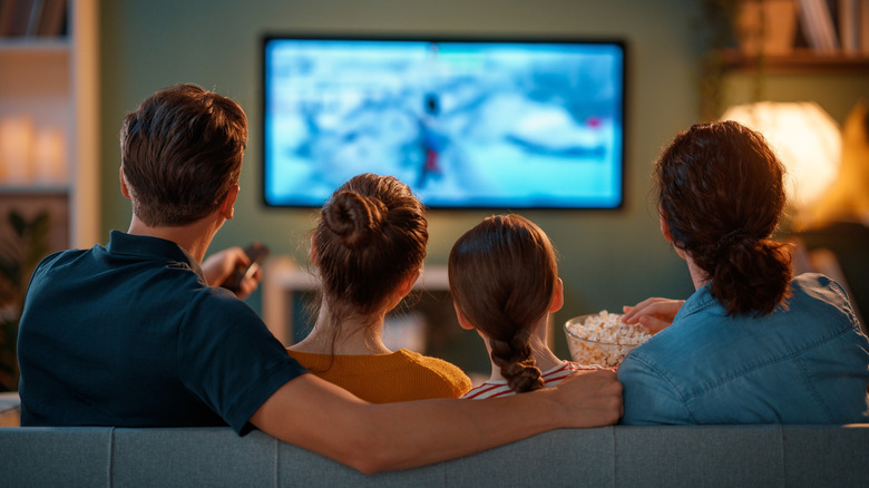 A family sitting on a sofa watching TV. The TV screen is blurred.