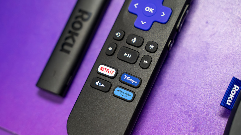 A Roku streaming stick and remote on a purple background