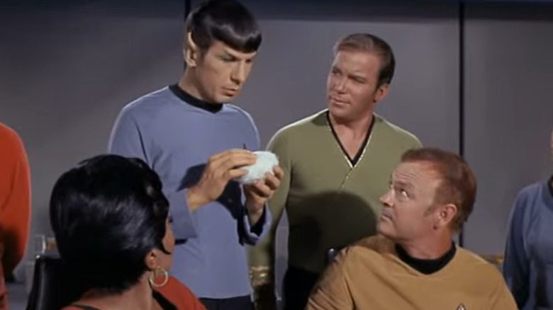 Spock holds a tribble, with the Enterprise crew around him