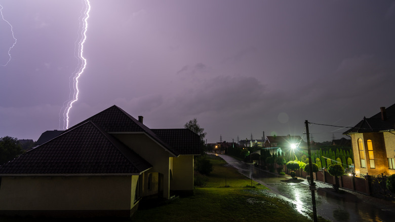 Houses illuminated during a storm with lightning in the background.