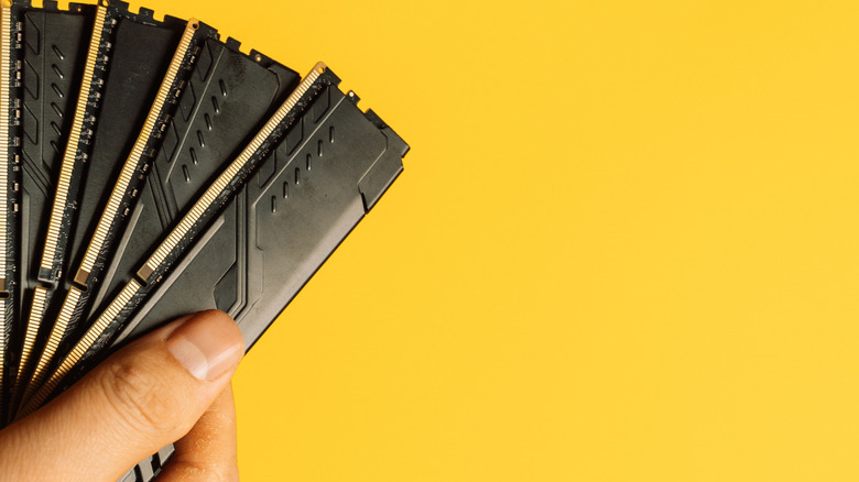 A person holding four sticks of DDR5 RAM on a mustard yellow background