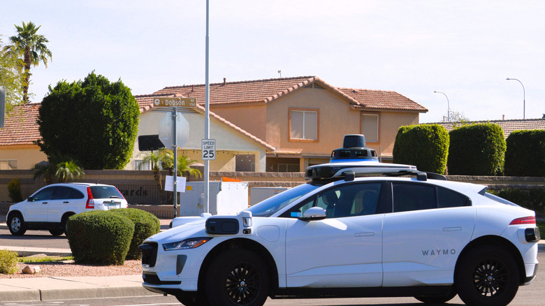 A Waymo driverless taxi operating on a public street in front of houses