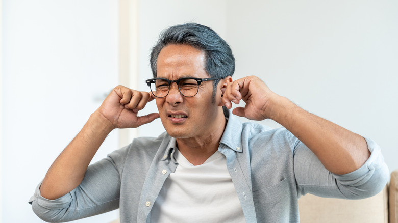 A man wearing glasses plugging his fingers into his ears to block incoming noise