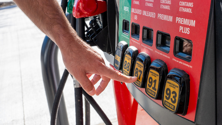 An individual's left hand is selecting 87 octane gasoline from a consumer fuel pump