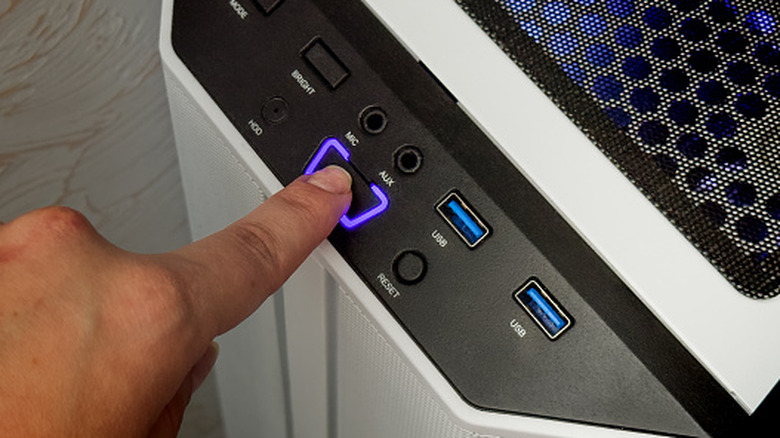 A person pressing a power button on a computer tower.