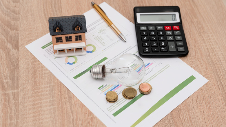 concept for power bill going up, little house on top of bill, calculator, pencil, lighbulb, and some change visible