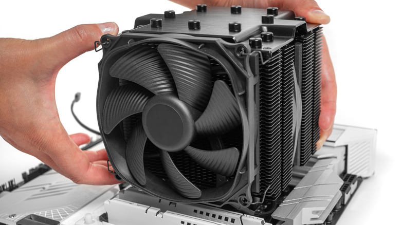 A person fitting a large CPU air cooler onto a white motherboard