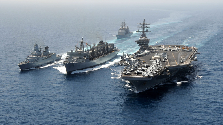 A US aircraft carrier mid-ocean with three smaller vessels off its starboard side
