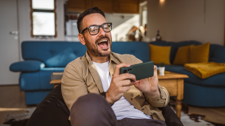 a man in his living room smiling and looking at his phone