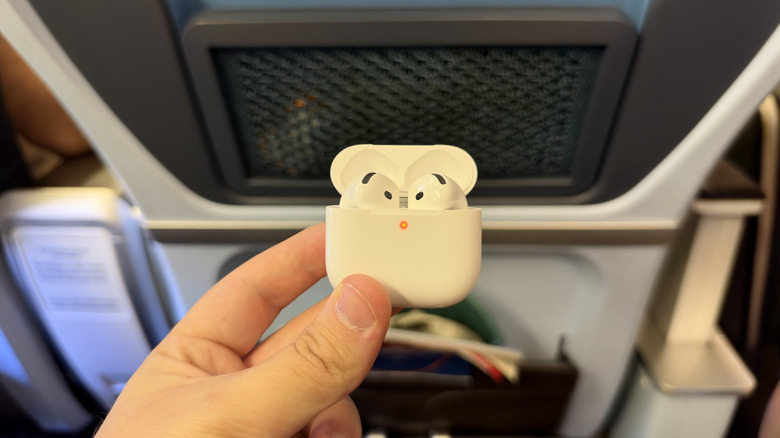 AirPods 5 in case being held in front of a plane seat