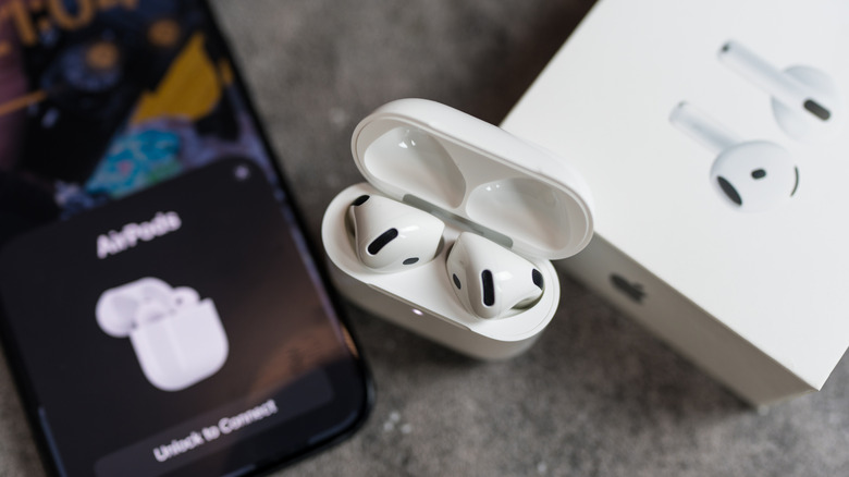 A top-down view of a pair of AirPods sitting in their charging case, the box for the product sits next to it as well as an iPhone displaying the AirPods connection window
