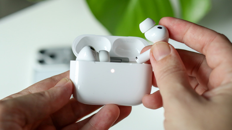 A person holding a pair of white AirPods Pro and case between their hands, their right hand is holding one of the AirPods