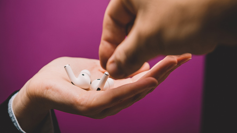 Hand grabbing one of the two AirPods from a hand