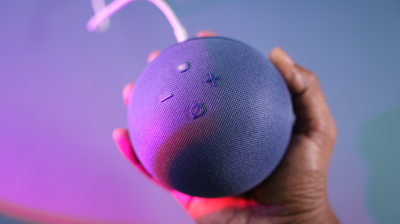 An Amazon Echo Dot held in someone's hands with a neon glow.