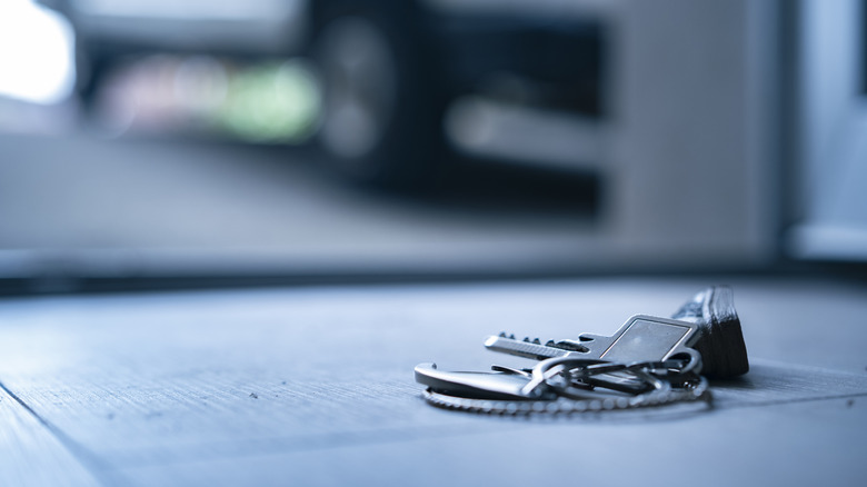 Keys on the ground in focus with a garage scene in the background.