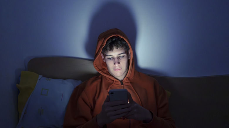 Young man illuminated by phone screen late at night