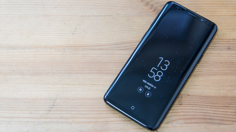 A Samsung phone with always-on display showing the data and time on a wooden surface