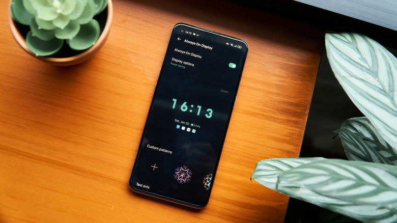 An Android phone showing the Always-On Display toggle and display options, on a table with plants on the side