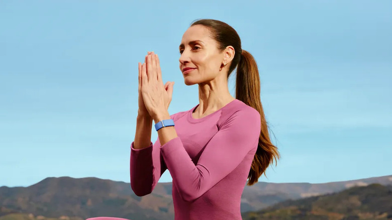 A woman doing yoga with a blue Fitbit Air on her wrist.