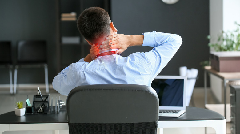 Man sitting at office desk and touching neck due to neck pain