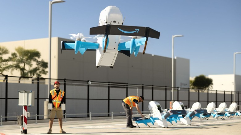 Amazon delivery drone mid take-off as amazon workers stand behind it.