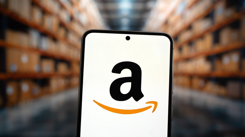 The Amazon logo on a phone in front of a warehouse of boxes