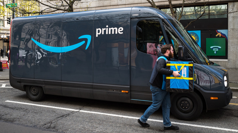 An Amazon driver carrying a tote of packages out of a Rivian electric delivery van.