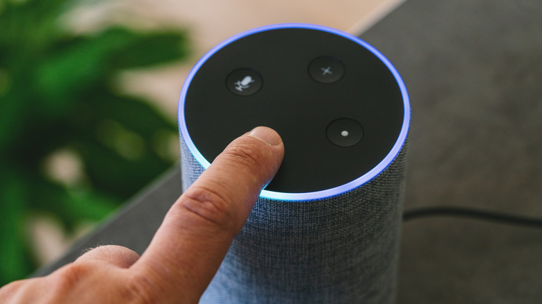 An individual placing their left-hand index finger on the minus button atop an Amazon Echo Plus, the Echo has a bright LED light that's blue and cyan