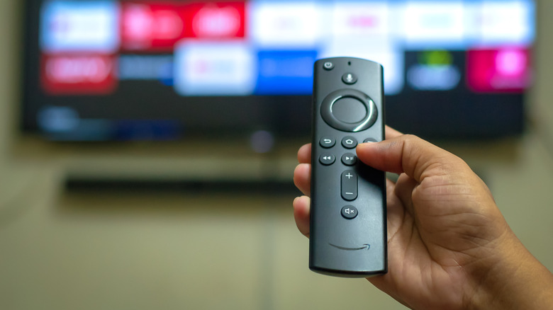 A person pointing an Amazon Fire TV remote at a TV screen.