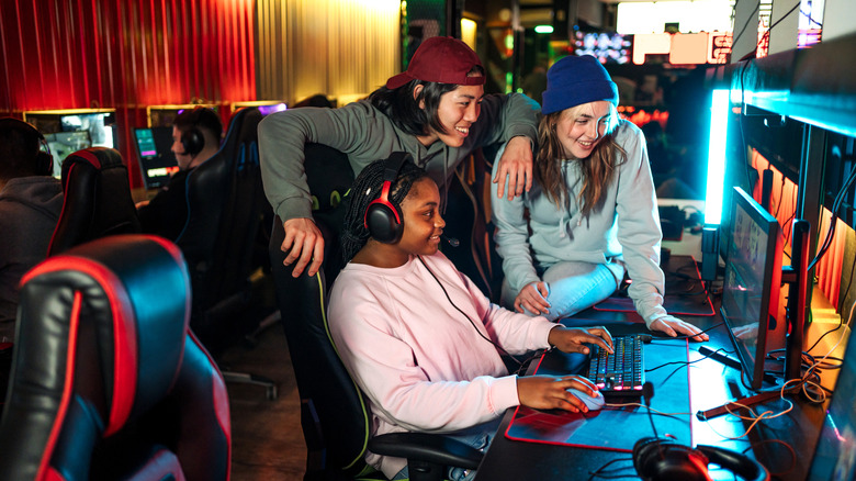 Three PC gamers gathered around a gaming PC.