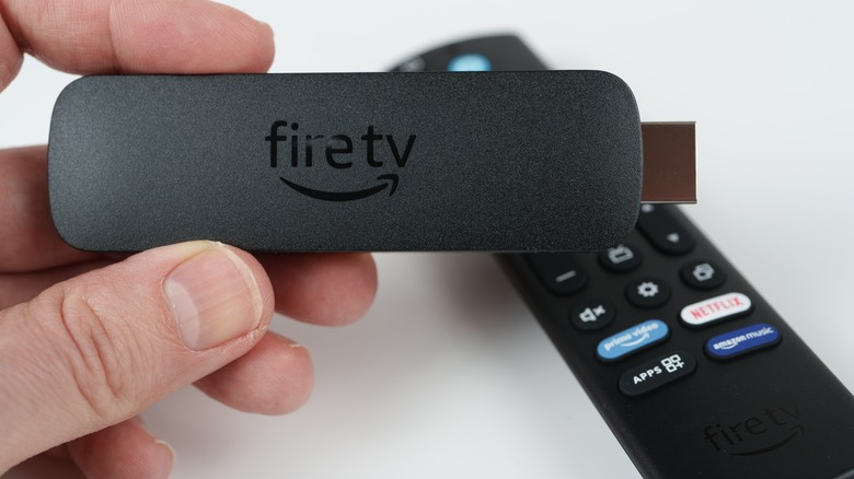 A hand holding a Fire TV Stick with a remote beside it.