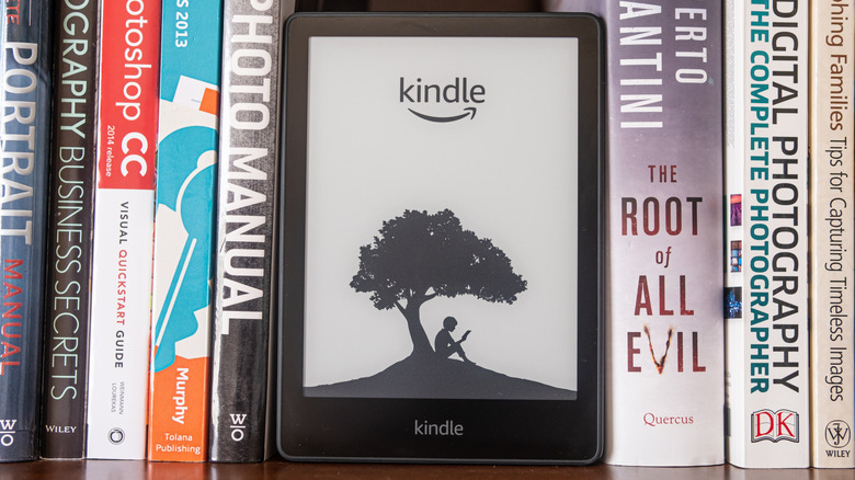A Kindle e-reader on a shelf alongside classic novels