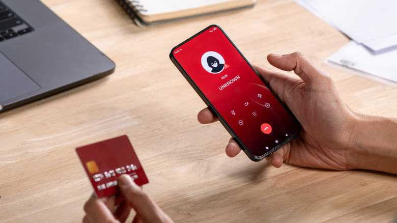 A person holding a credit card next to a phone with an unknown caller