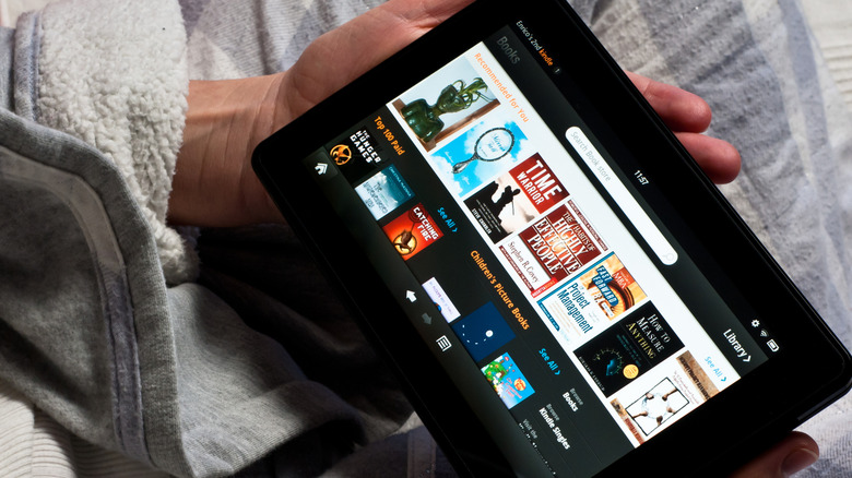 person in bed and a robe uses the Amazon Kindle Fire to look for something to read or watch