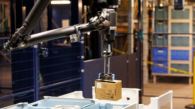 The black robotic arm of Blue Jay, Amazon's warehouse robot, picks a small package out of a bin and begins to move it
