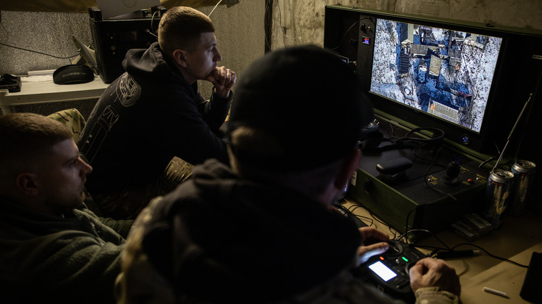 Three Ukrainian soldiers sit at a computer screen displaying footage of the drone they're operating.