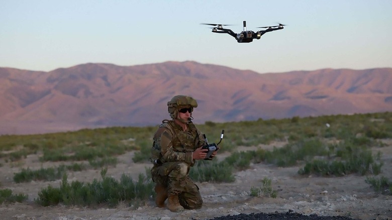 A U.S. soldier crouches while operating a quadcopter drone in a sparse, mountainous plain at the Joint Readiness Training Center at Fort Polk, Louisiana.