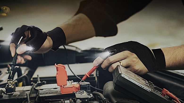 Someone using Parigo hands-free gloves with LED lights built in to work on a car engine.