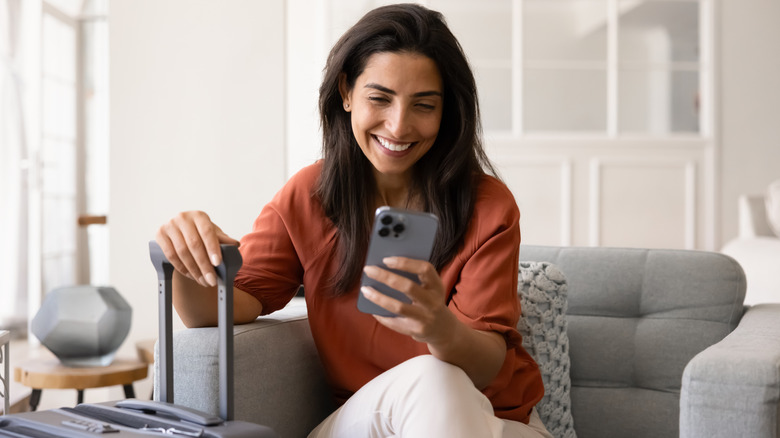 A woman looking at her phone with her hand resting on her luggage.