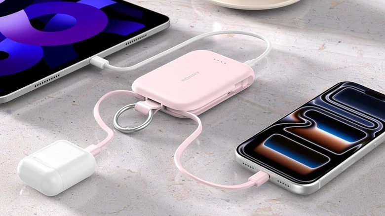 A closeup of a pink Rorry 5000mAh Portable Charger Power Bank charging multiple devices, including an iPhone, AirPods, and an iPad