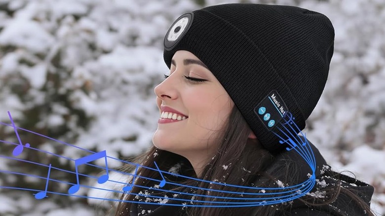 A person with long brown hair smiling while they wear the Topiei Bluetooth Beanie Flashlight Hat